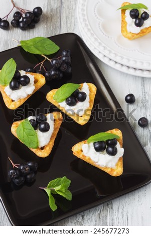 canape with cottage cheese, black berries of mountain ash and fresh mint leaves on a white wooden background. light sweet snack.