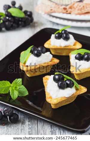 canape with cottage cheese, black berries of mountain ash and fresh mint leaves on a white wooden background. light sweet snack.  selective focus