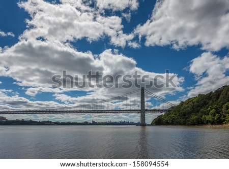 George Washington Bridge linking New Jersey and Manhattan, NYC, spanning Hudson River. Clouds and the river enhanced by the late summer light.  Manhattan skyline in the background.