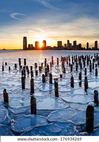 Wood pilings from New York old pier sticking out through the ice on Hudson River at sunset with Jersey City buildings in the distance. Frozen Hudson River January 2014.