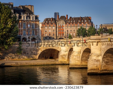 Paris at dawn. Pont Neuf across the River Seine and the buildings on the west end of Ile de la Cite are slowly waking to morning's warm sun rays. Urban view of Paris and its architecture.