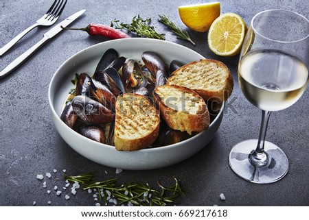 mussels in white wine sauce with glass of white wine  white bread toasts, decorated with hilly pepper, lemon and sea salt