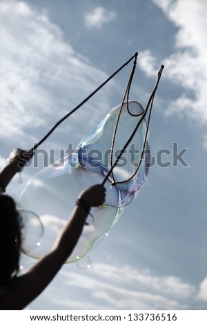 An anonymous woman making giant soap bubbles against cloudy sky background.