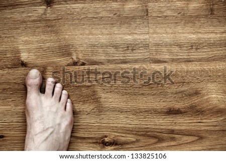 Bare and somewhat hairy right foot of an adult caucasian man, on brown parquet floor. Viewed from directly above.