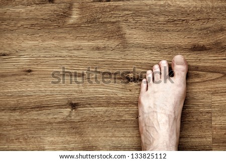 Bare and somewhat hairy left foot of an adult caucasian man, on brown parquet floor. Viewed from directly above.