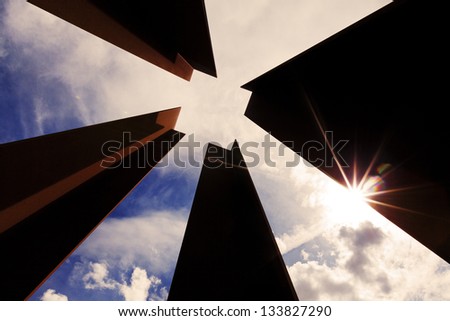 Low angle view of four columns that together create a negative space in the shape of a square, on the background of cloudy sky at the afternoon.