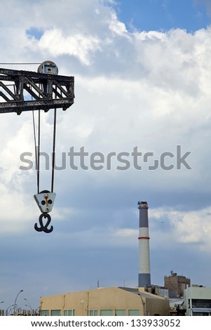 A vintage run-down crane in the Tel-Aviv harbour with a warehouse and the chimney of \'Reading\' fossil fuel power plant in the background. Shot in a lovely winter day with dramatic clouded sky.