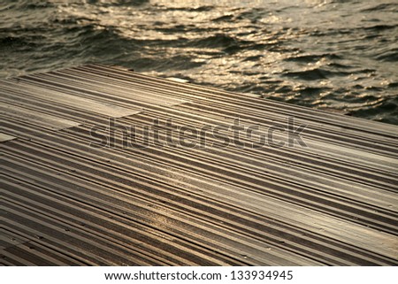 A wooden deck completely soaked wet by the waves of the gushing sea hitting against it, on a winter day.