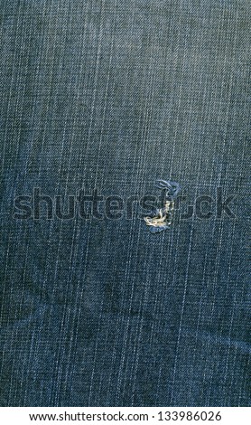 High resolution scan of blue denim fabric with a large rip and a general worn-out look.