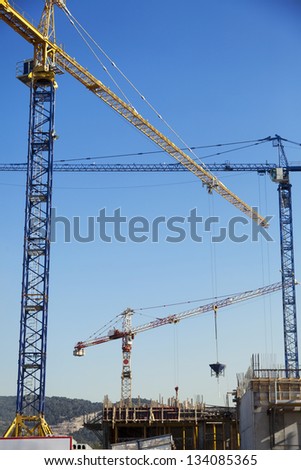 Low angle view of three tower cranes in a rural construction site, on a clear day in a rural hills area.