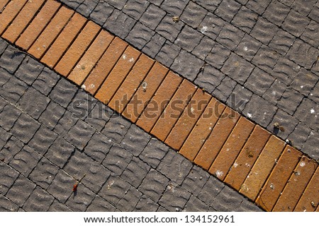 Gray floor tiles with wavy/rippled texture  and red bricks lit by direct afternoon sun. Good as background.