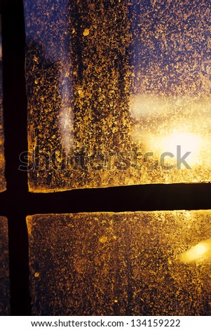 Afternoon yellow sun is back-lighting a window stained with drop marks, accentuating the texture and shapes.
