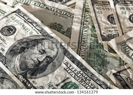A close up high angle view of a very large amount of crumpled 100 US$ money notes in a bulky mess, with warm & contrasty lighting.