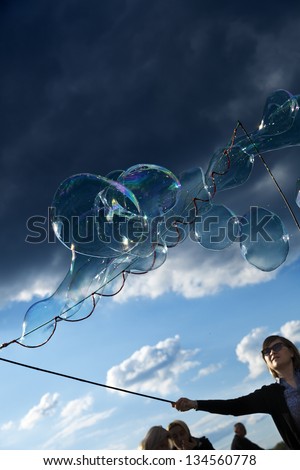 BERLIN - JUNE 10th: A woman making giant soap bubbles on an early summer afternoon at Mauerpark, with the park\'s crowd all around on June 10 2012 in Berlin, Germany.