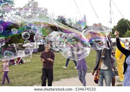 BERLIN - JUNE 10: A group of young adults making giant soap bubbles on a summer day at Mauerpark, with the flea market in the background on June 10 2012 in Berlin, Germany.