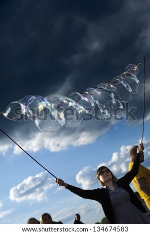 BERLIN - JUN 10: A young woman making giant soap bubbles on an early summer day at Mauerpark, with the park\'s crowd all around on June 10 2012 in Berlin, Germany.