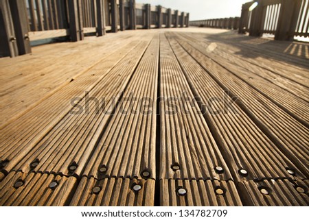 A wooden deck footpath in the sunlight, diminishing perspective.