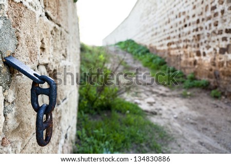 Two blue chain links hanging off of a stone wall, suggesting that the blurry path in the background is sometimes closed.
