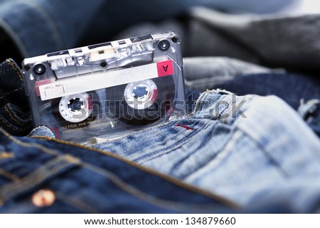 A blank audio cassette laid on the background of various pairs of jeans pants.  Very shallow depth of field