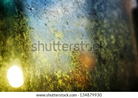 A dirty glass window back lit by a ray of the afternoon sun, inducing a chiaroscuro light affect in combination with the unfocused urban setting.
