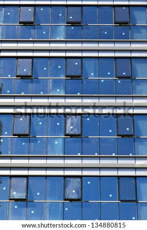 Frontal view of a building\'s curtain wall, with most its windows slightly opened. The stickers on the windows indicate this building is in the process of construction.