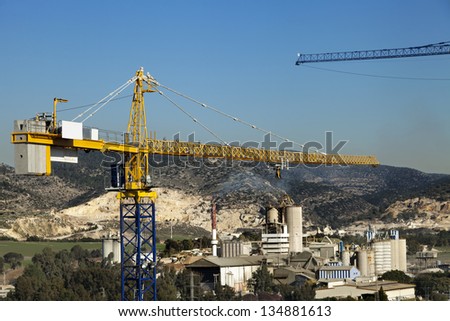 The top part of a tower crane raising above an industrial park located in rural surroundings.