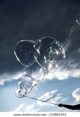 A young adult woman making giant soap bubbles on an early summer Sunday afternoon at Mauerpark, with dramatic sky in the background.