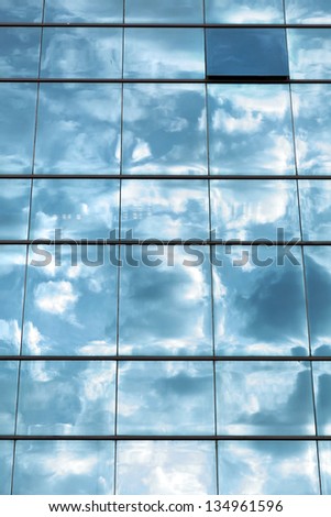 Cloudy sky reflecting off an office building\'s curtain wall made of identical square windows, with one window open.