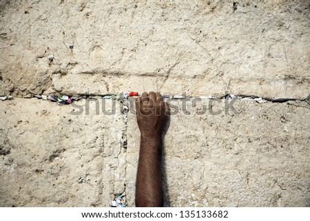 The left hand of an adult male placing a note in the cracks of the holy Western Wall in the old city of Jerusalem, Israel.