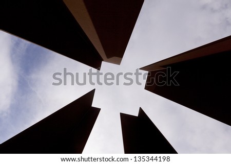 Low angle view of four columns that together create a negative space in the shape of a square, on the background of cloudy sky at the afternoon.