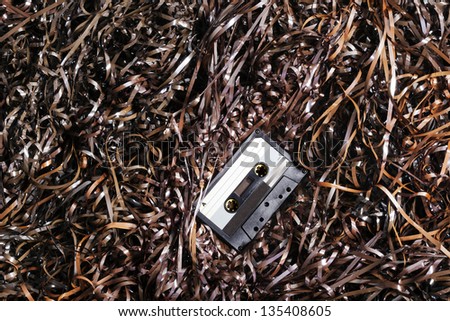 Black recordable plastic audio cassette resting on a large amount of magnetic audio tape.