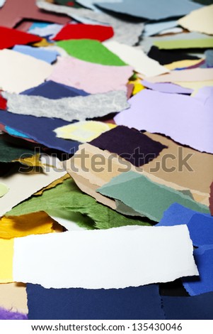 Torn long white fiber paper on the background of a large group of torn pieces of paper in a variety of colors. Good as copy space for text.