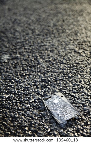 Close up of a shattered plastic cellphone panel laying on asphalt road.