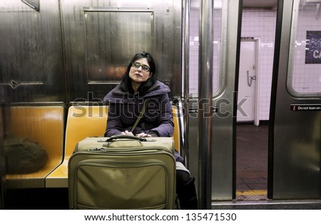 An adult woman with luggage sitting in the Brooklyn bound (downtown) A train subway in Manhattan, the door closing and train about to depart the station.