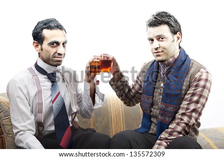 Two adult man wearing old-man clothes and makeup, sitting on a used up vintage sofa. Both of them are smiling at the camera while toasting their tea glasses. Isolated on white background.