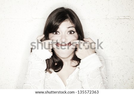 Portrait of a beautiful young woman making a funny face; her fingers pulling her mouth as upwards as possible.