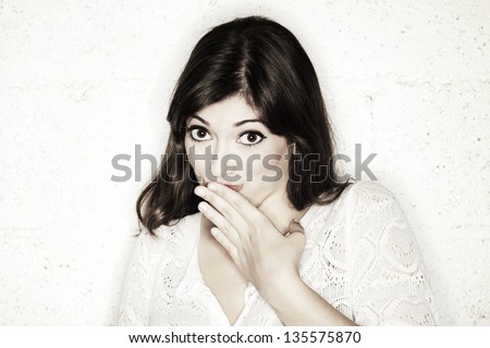 Portrait of a beautiful young woman looking at the camera with her hand covering her mouth. Looks like she is feeling shy towards something, or maybe guilty. Either way, she is very cute.