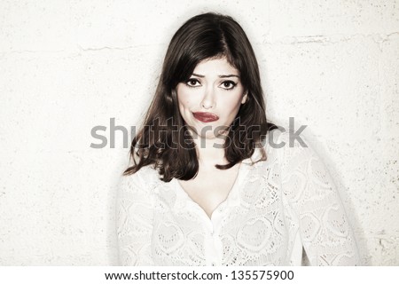 Portrait of a beautiful young woman looking at the camera with an exaggerated frowny expression, looking like she can't decide on a certain matter, or maybe reacting reluctantly to something.