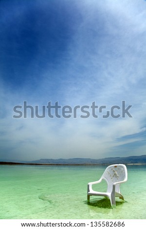 A lone salt covered plastic easy chair in the shallow waters of the world famous Dead Sea, Israel.