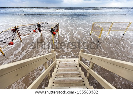 Wide angle view of the tides at the beach on a stormy winter day, as seen from the top of the stairs belonging to a lifeguard hut.