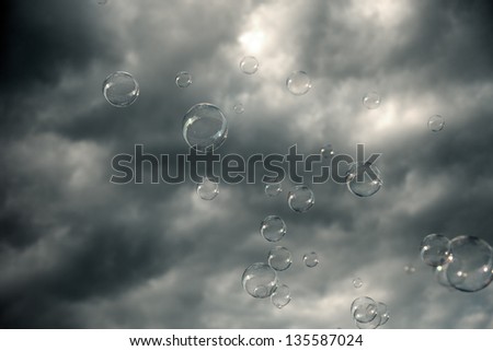 Soap sud bubbles floating in the air on the background of dramatic sky with heavy gray clouds.