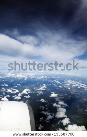 Aerial view of clouds over green land features, with jet engine in the front.