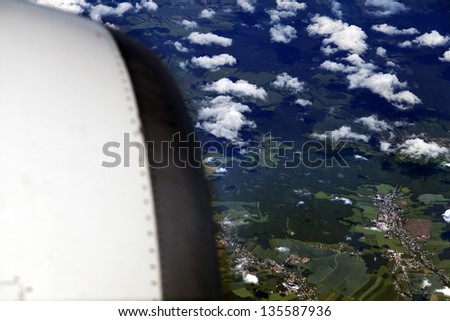 Aerial view of clouds over green land features, with defocused jet engine in the front.