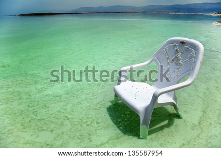 A lone salt covered plastic easy chair in the shallow waters of the world famous Dead Sea, Israel.