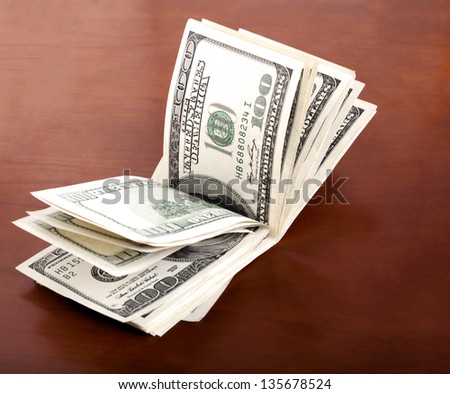 A folded stack of 100 US$ money notes on brown wooden background.