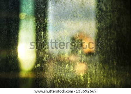 A dirty glass window backlit by a ray of the afternoon sun, inducing a chiaroscuro light affect in combination with the defocused urban setting.