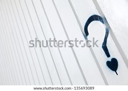 A blue graffiti in the shape of a question mark with a small heart instead of the dot, on a white metal wall with creases pattern.
