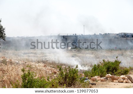 BIL\'IN, PALESTINE - MAY 17: A cloud of tear gas flying in the wind by the wall of separation between Palestine and Israel, with Israeli soldiers behind the wall on May 17, 2013 in Bil\'in, Palestine.