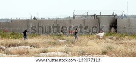 BIL\'IN, PALESTINE - MAY 17: Palestinian youths throwing rocks on the Israeli army force behind the wall of separation between them on May 17, 2013 in Bil\'in, Palestine.