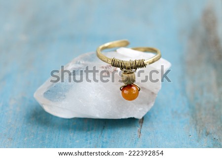 Still life of a hand made tribal ethnic ring resting on a crystal on light blue background.